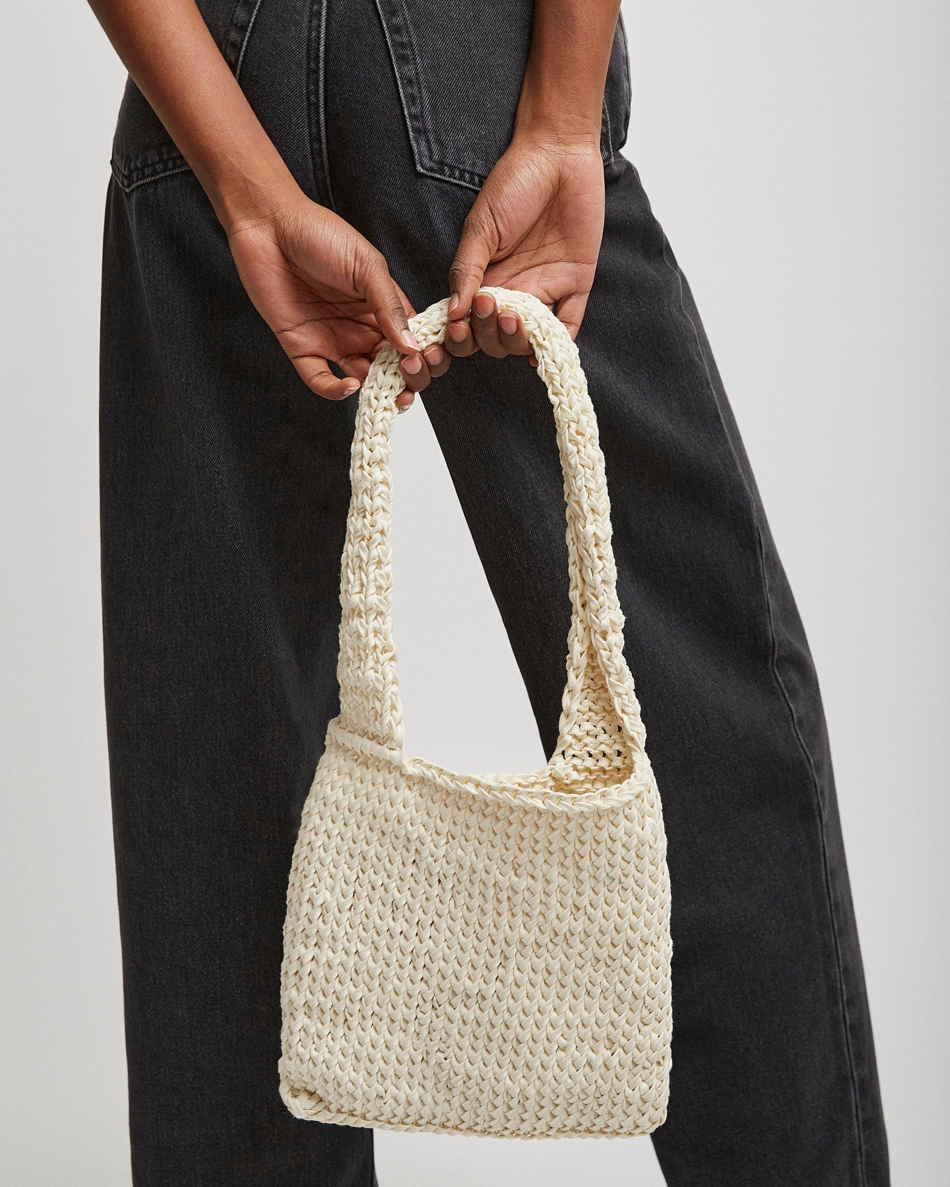 Person holding a woven handbag against a plain background