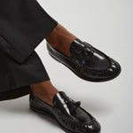 Black loafers worn with black pants on a light gray background