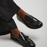 Black loafers worn with black pants on a light gray background