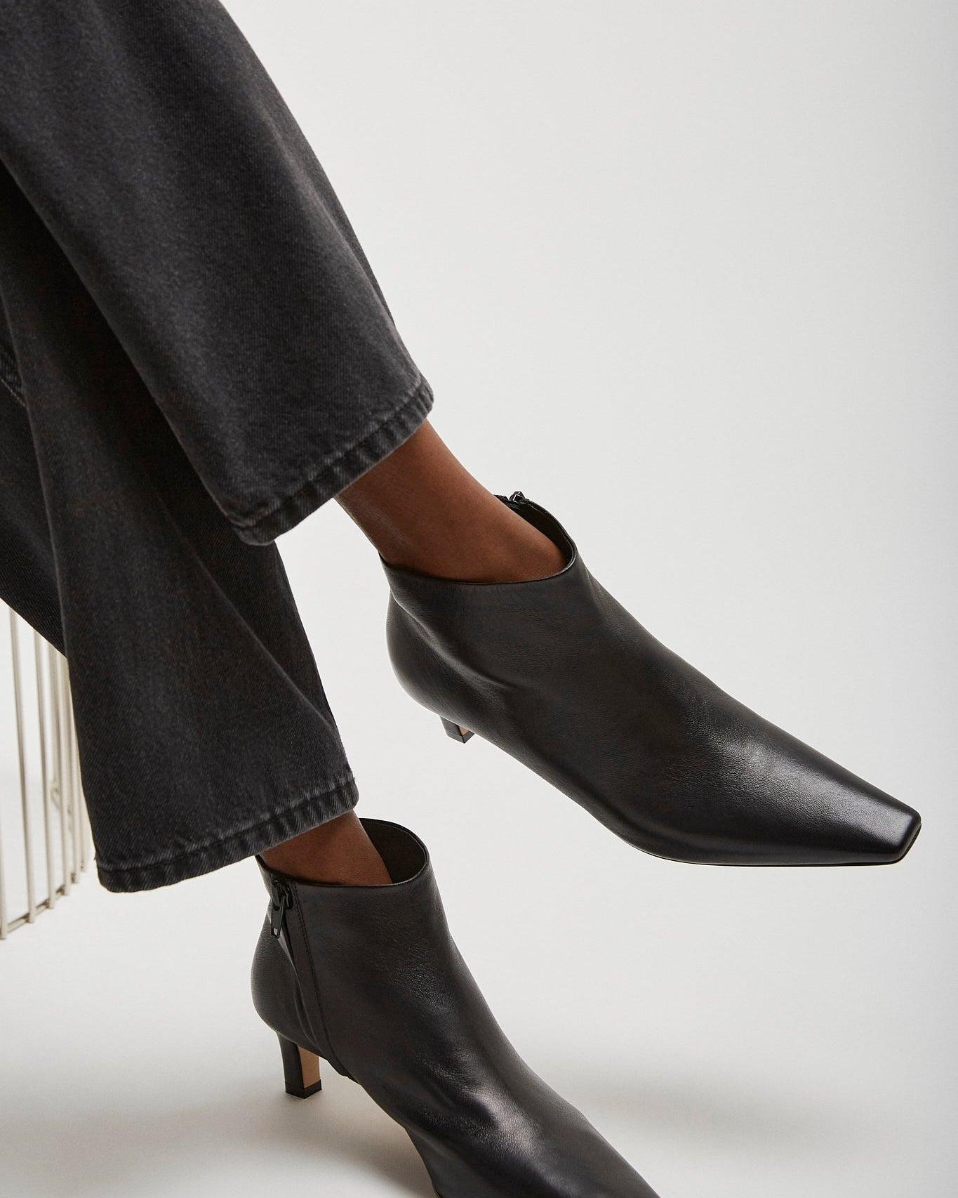 Black ankle boots worn with dark jeans on a light gray background