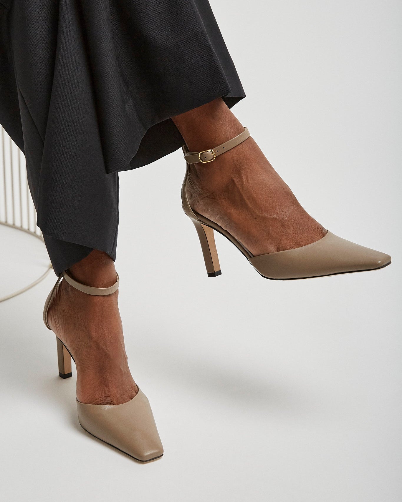 Brown high-heeled shoes worn with black pants on a white background