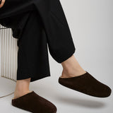 Person wearing black pants and brown slippers on a light gray background