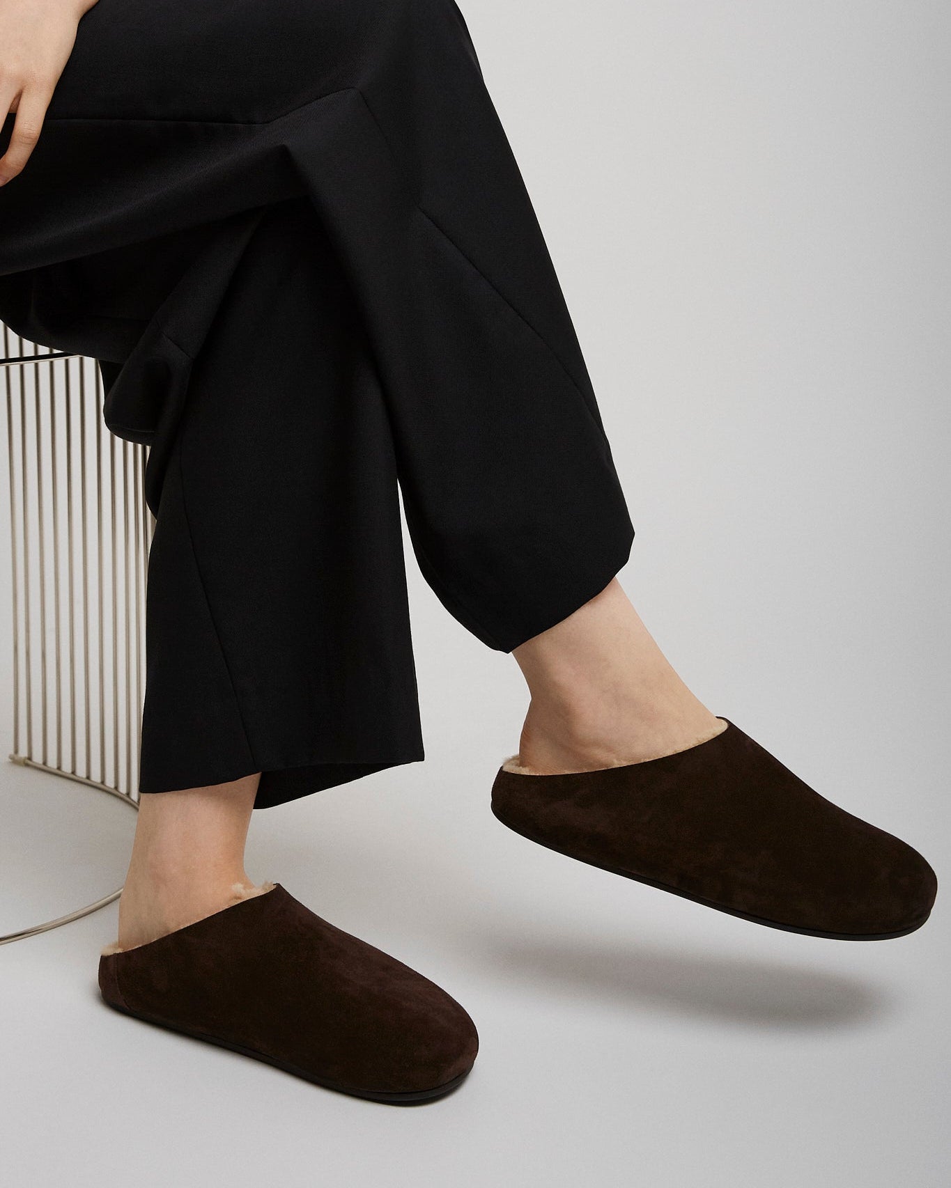 Person wearing black pants and brown slippers on a light gray background