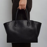 Person holding a black leather handbag against a plain background