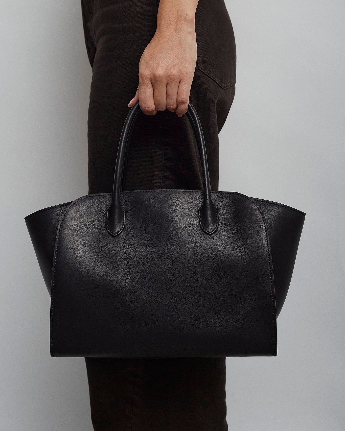 Person holding a black leather handbag against a plain background