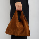 Brown handbag held by a person wearing black pants against a white background