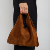 Brown handbag held by a person wearing black pants against a white background