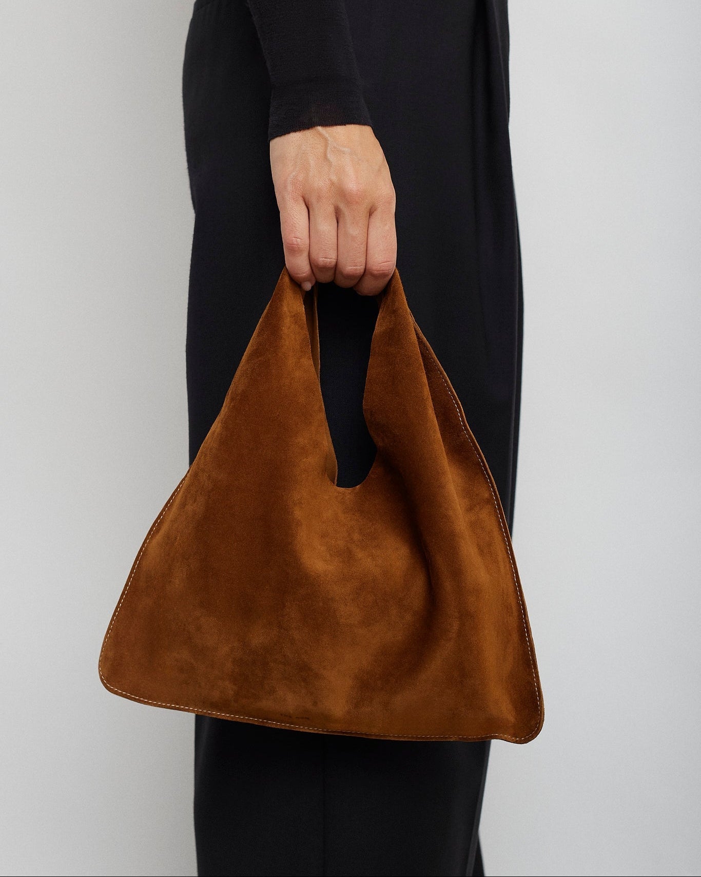 Brown handbag held by a person wearing black pants against a white background