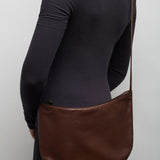 Person wearing a black long-sleeve shirt with a brown leather bag over one shoulder against a plain background.