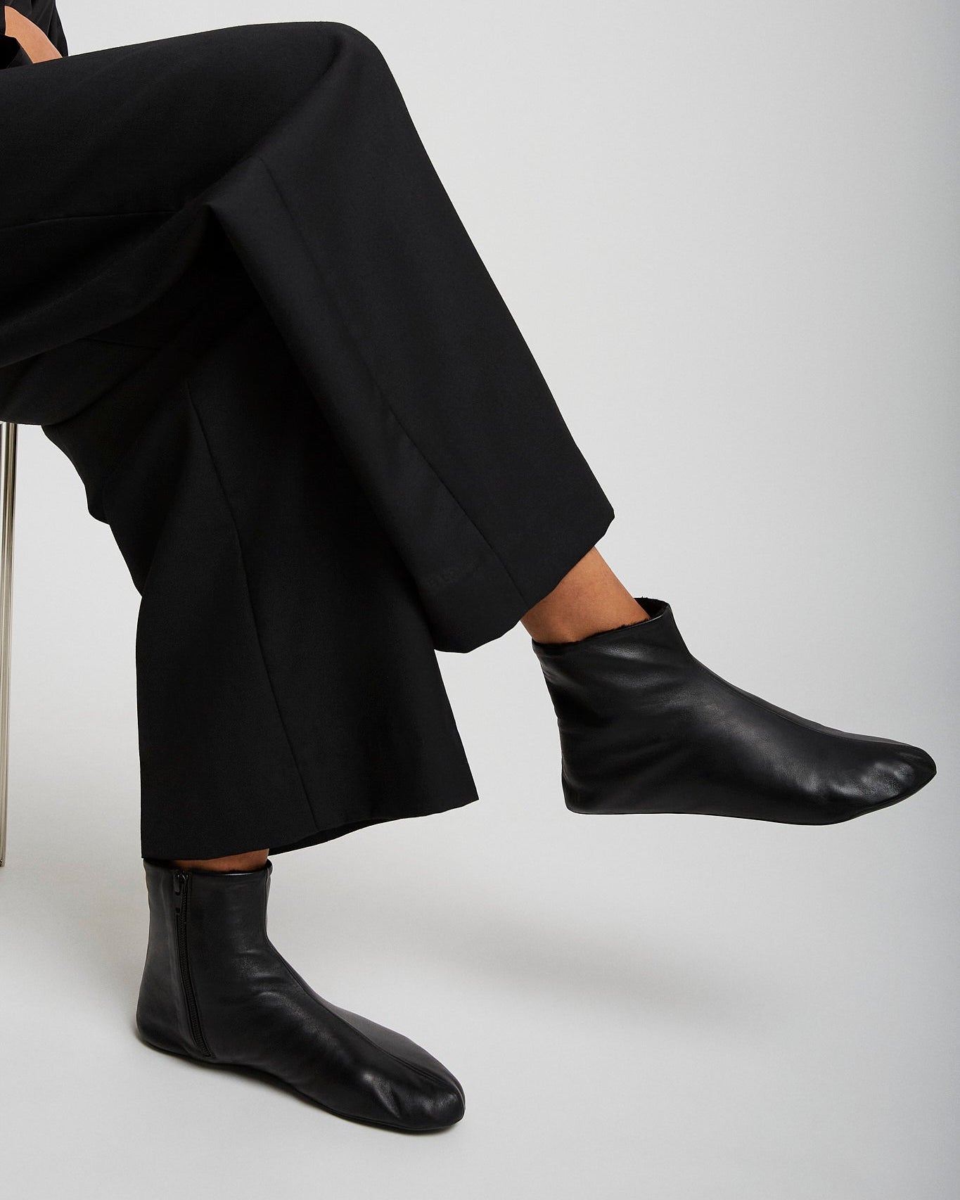 Person wearing black leather ankle boots and pants on a white background