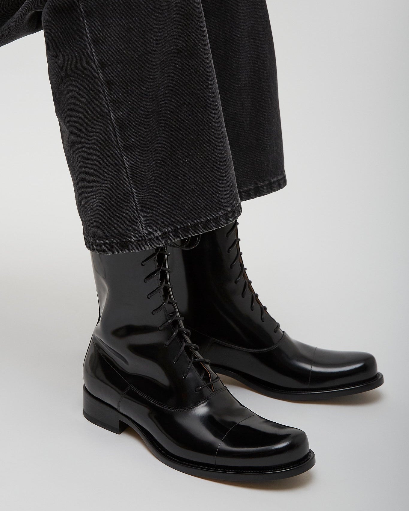 Black leather boots worn with black pants on a light gray background