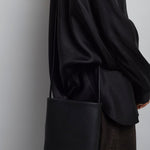 Person wearing a black coat holding a black bag against a plain background