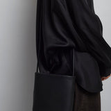 Person wearing a black coat holding a black bag against a plain background