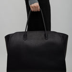 Person holding a black leather bag against a plain background
