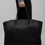 Person holding a black leather bag against a plain background