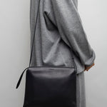Person wearing a gray coat holding a black bag against a plain background