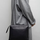 Person wearing a gray coat holding a black bag against a plain background