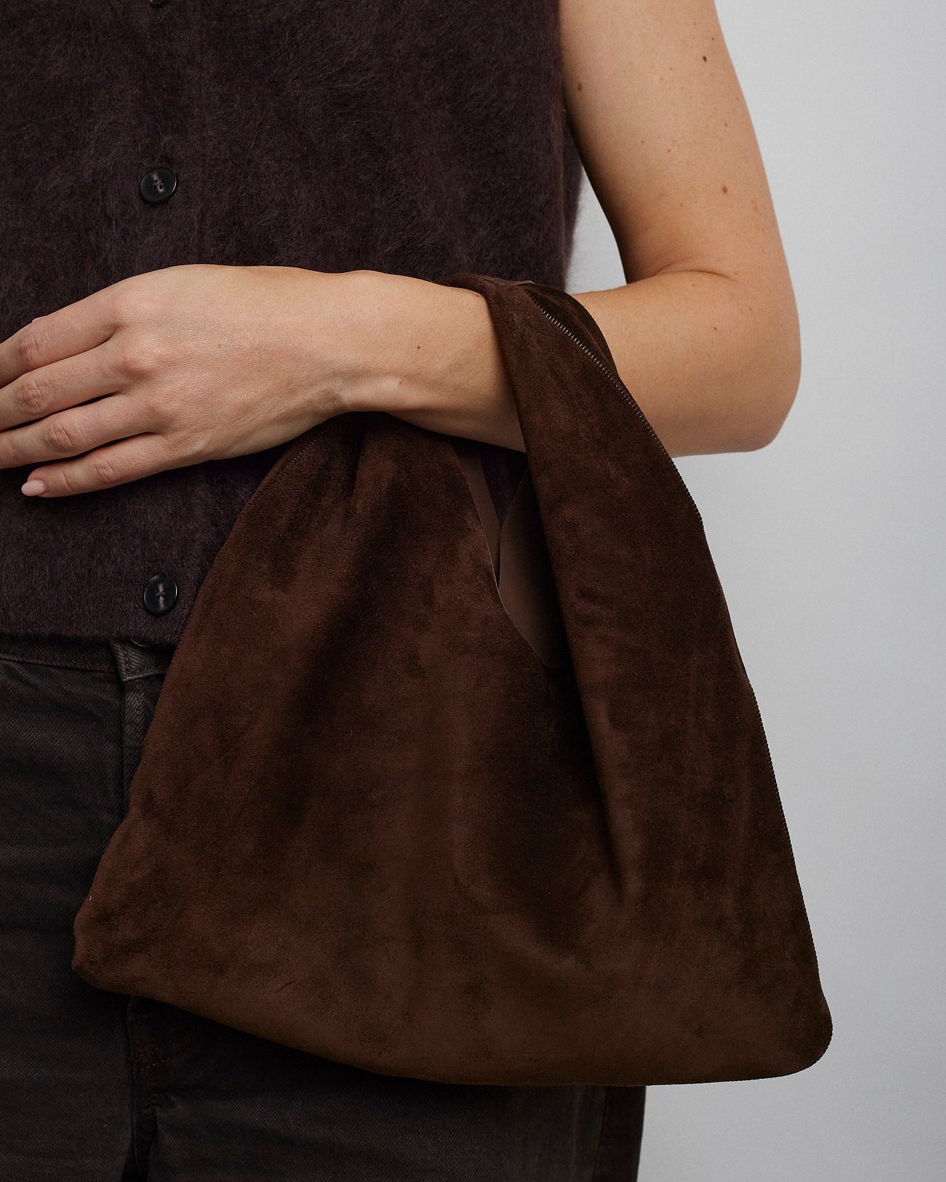 Brown suede bag held by a person against a white background