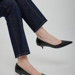 Person wearing dark blue jeans and black pointed-toe shoes on a light gray background