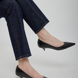 Person wearing dark blue jeans and black pointed-toe shoes on a light gray background