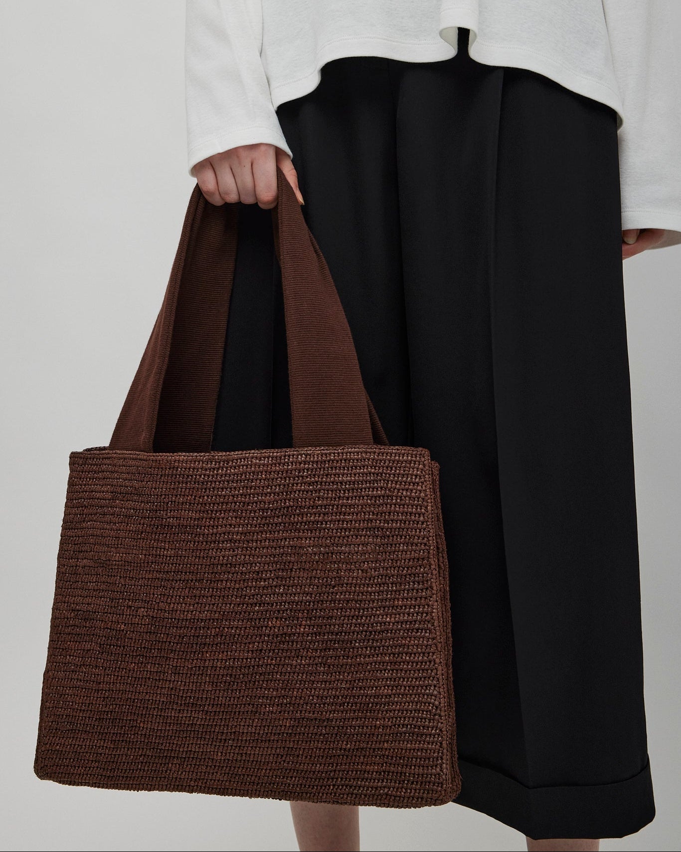 Person holding a brown woven bag against a plain background