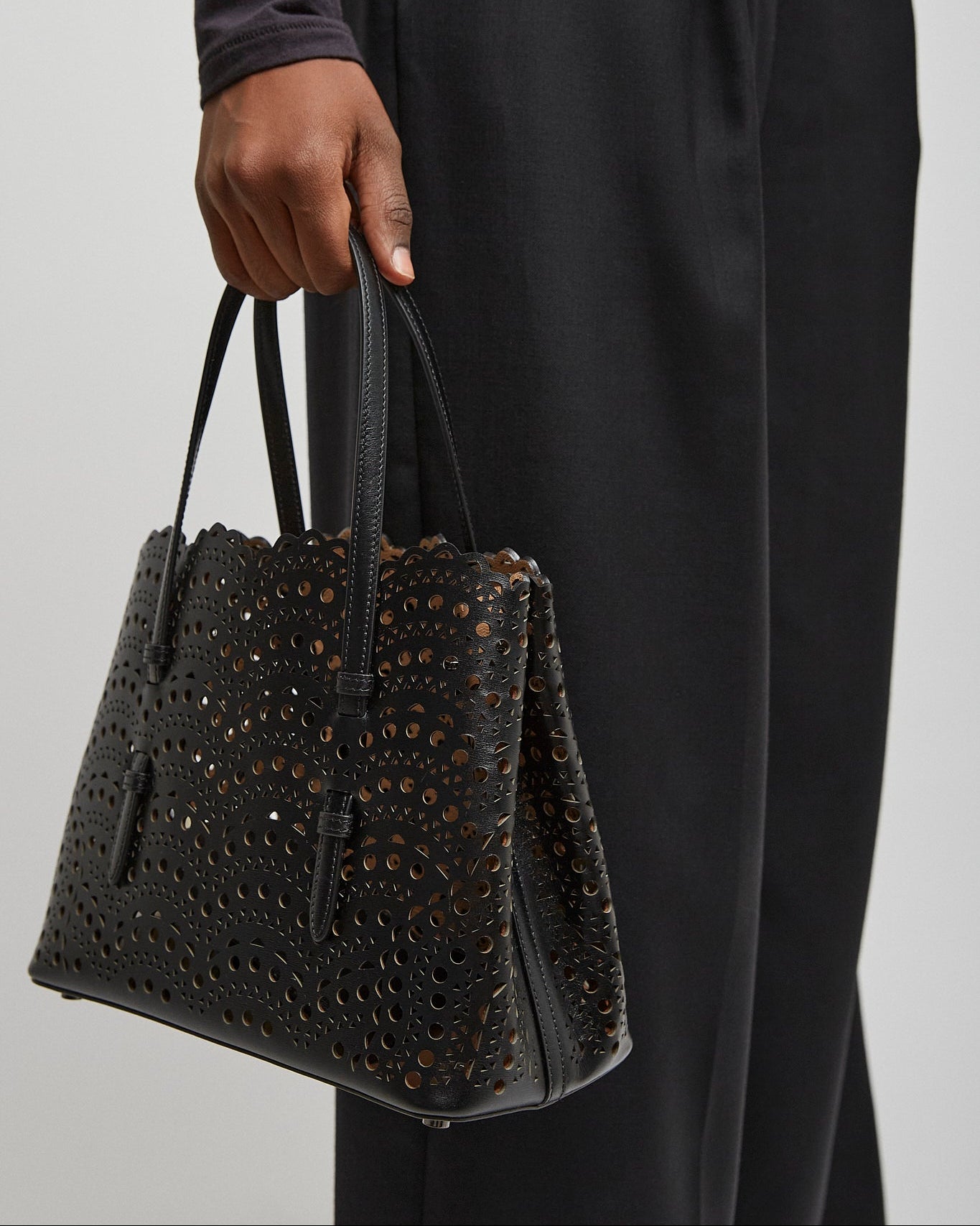 Person holding a black textured handbag against a plain background