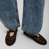 Person wearing blue jeans and brown perforated shoes on a light gray background
