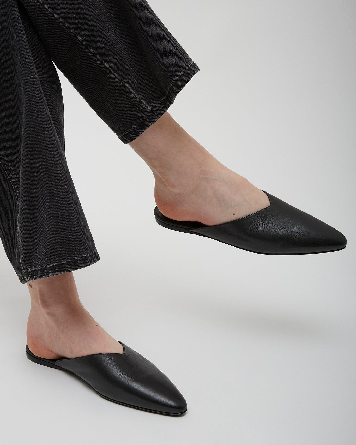 Person wearing black leather mules with black pants on a light gray background