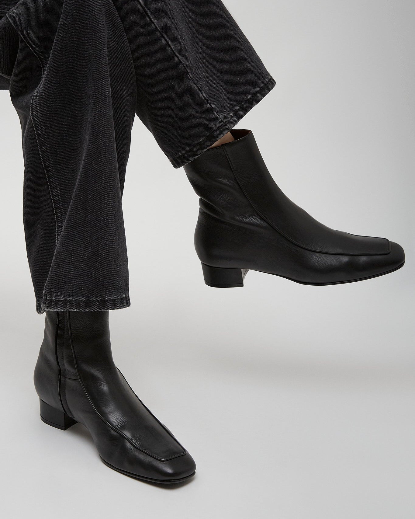 Black leather ankle boots worn with black jeans on a light gray background