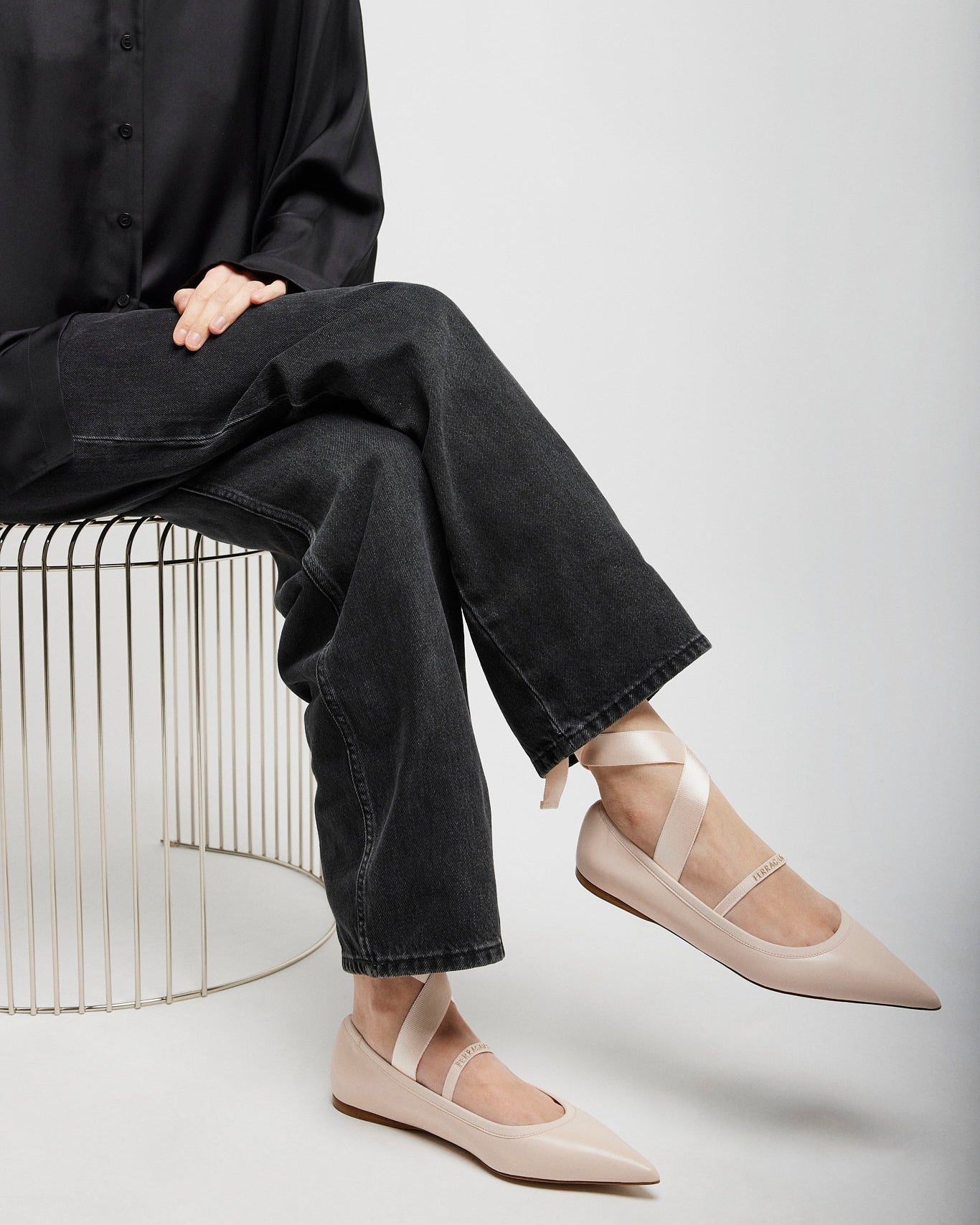 Person wearing black shirt and jeans with beige flats sitting on a white background