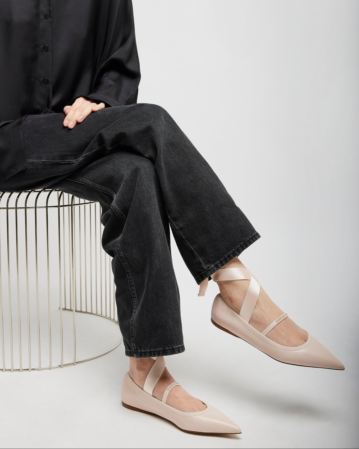 Person wearing black shirt and jeans with beige flats sitting on a white background
