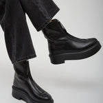 Person wearing black leather boots and black pants on a light gray background