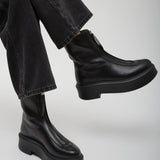 Person wearing black leather boots and black pants on a light gray background