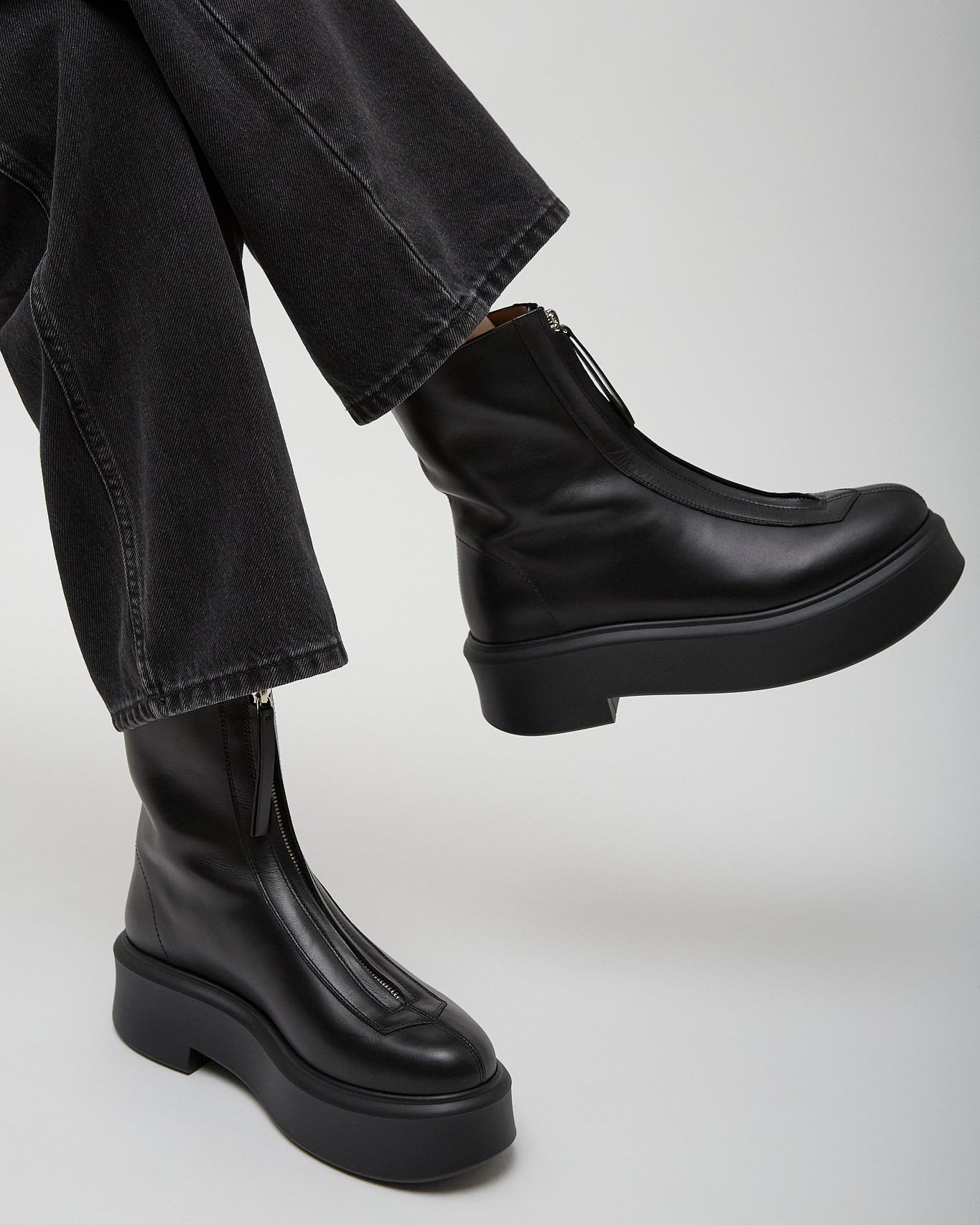 Person wearing black leather boots and black pants on a light gray background