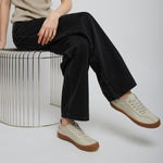 Person wearing a beige tank top, black pants, and beige sneakers sitting on a metal stool.