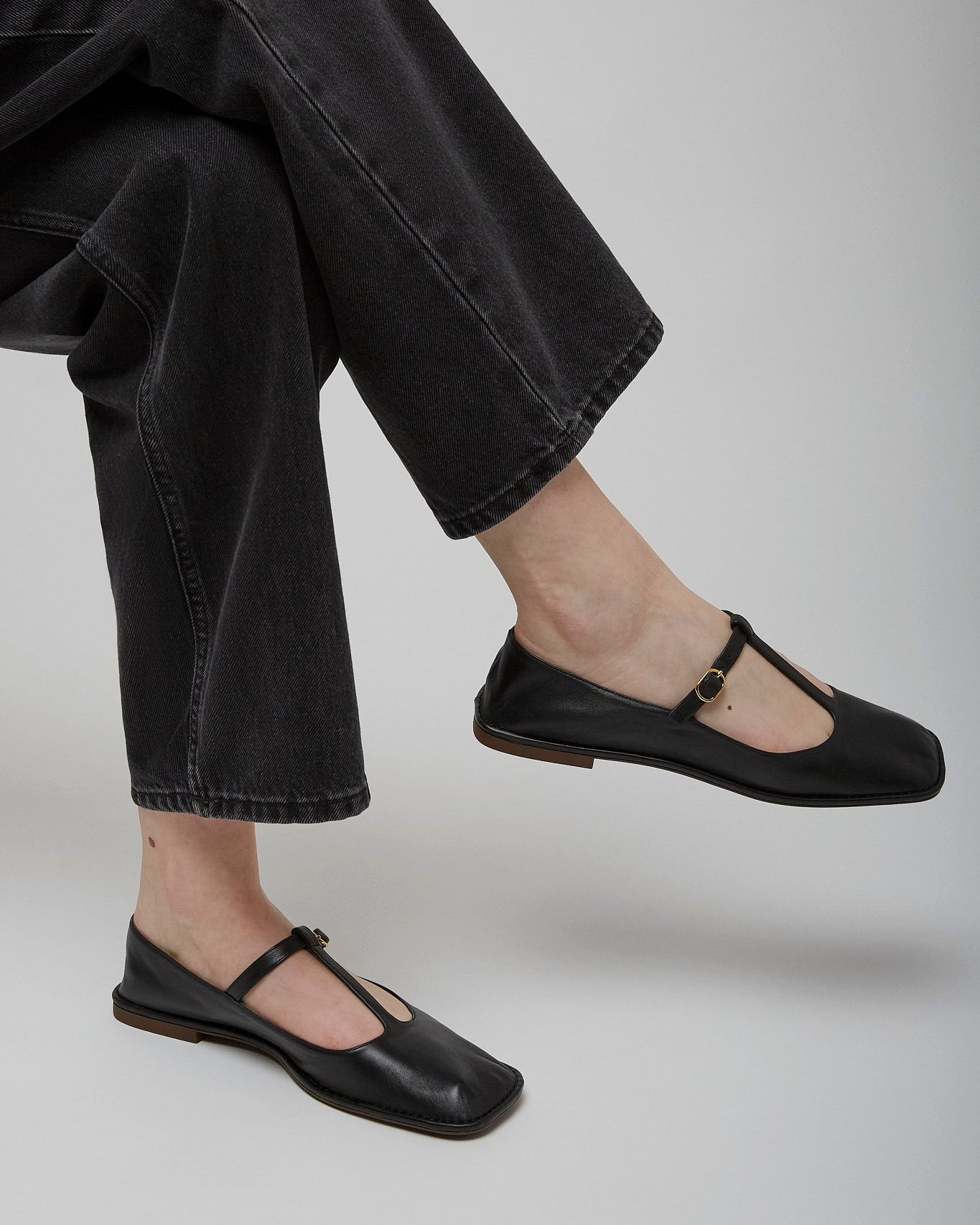 Person wearing black flat shoes and black jeans on a light gray background